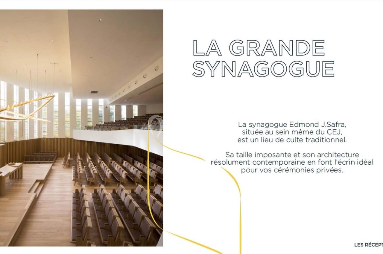 Vue intérieure d'une synagogue moderne avec des rangées de sièges en bois, un éclairage suspendu et de grandes fenêtres.