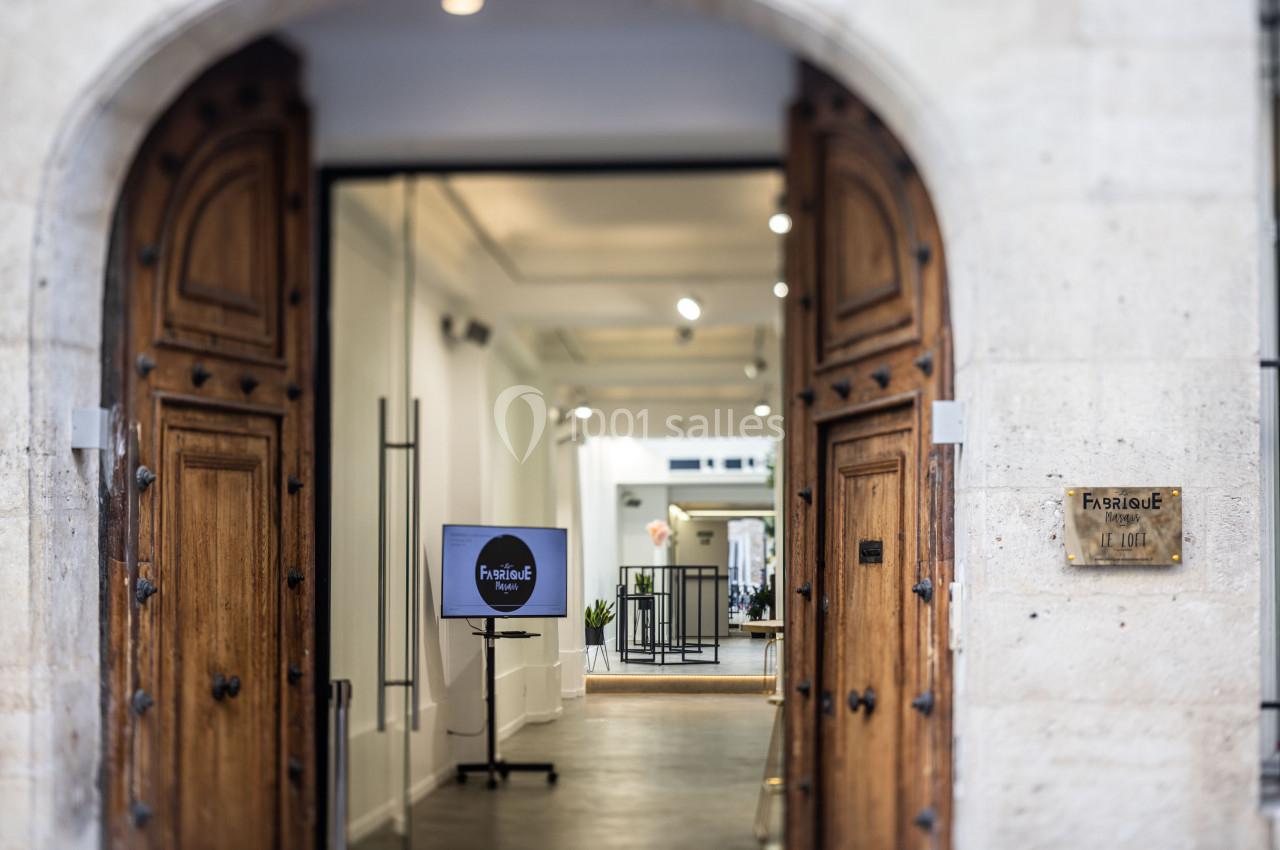 Entrée d'un bâtiment avec des portes en bois ouvertes, menant à un espace intérieur lumineux et moderne.