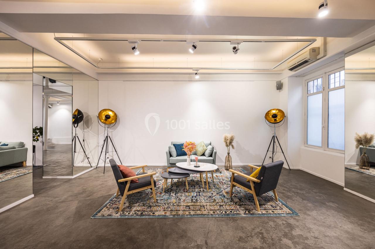 Salon moderne avec canapé, fauteuils, tables basses, tapis coloré, lampes dorées et grands miroirs sur les murs.