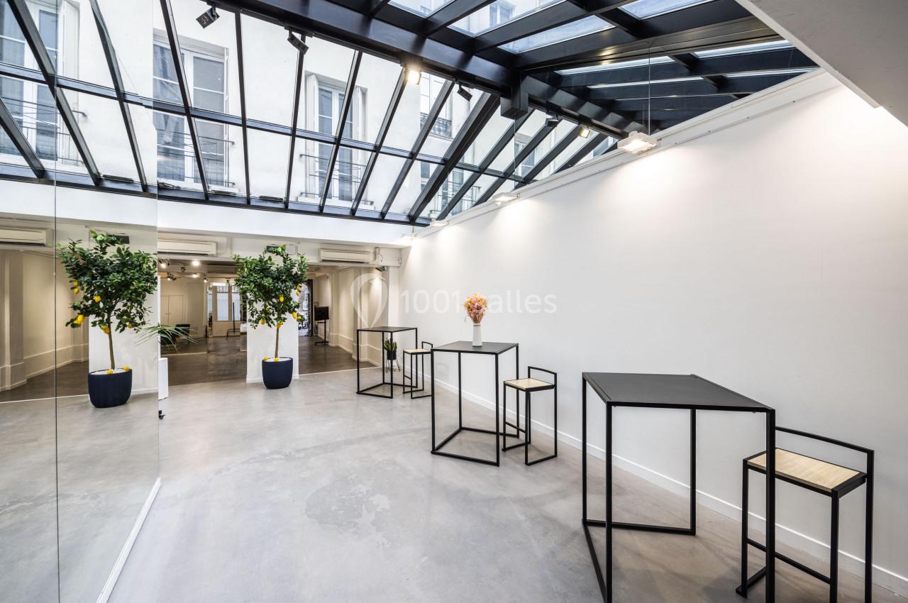 Salle lumineuse avec verrière, murs blancs, mobilier minimaliste en métal noir et plantes en pots.