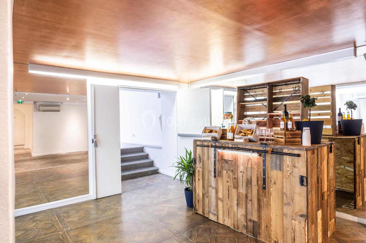 Espace intérieur lumineux avec comptoir en bois, plantes décoratives et accès à une salle adjacente.