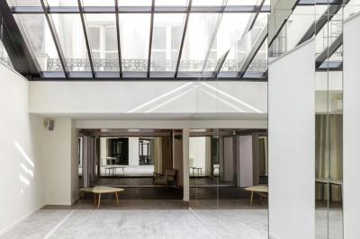 Salle lumineuse avec verrière, murs blancs, sol clair et mobilier minimaliste comprenant une table basse et un fauteuil.