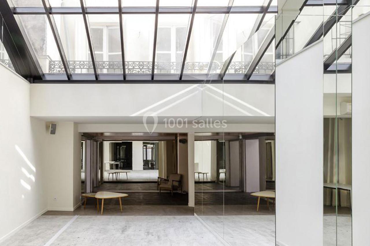 Salle lumineuse avec verrière, murs blancs, sol clair et mobilier minimaliste comprenant une table basse et un fauteuil.