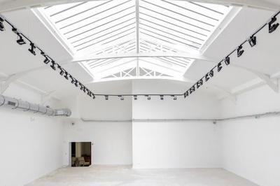 Salle lumineuse avec verrière, murs blancs, sol clair et mobilier minimaliste comprenant une table basse et un fauteuil.