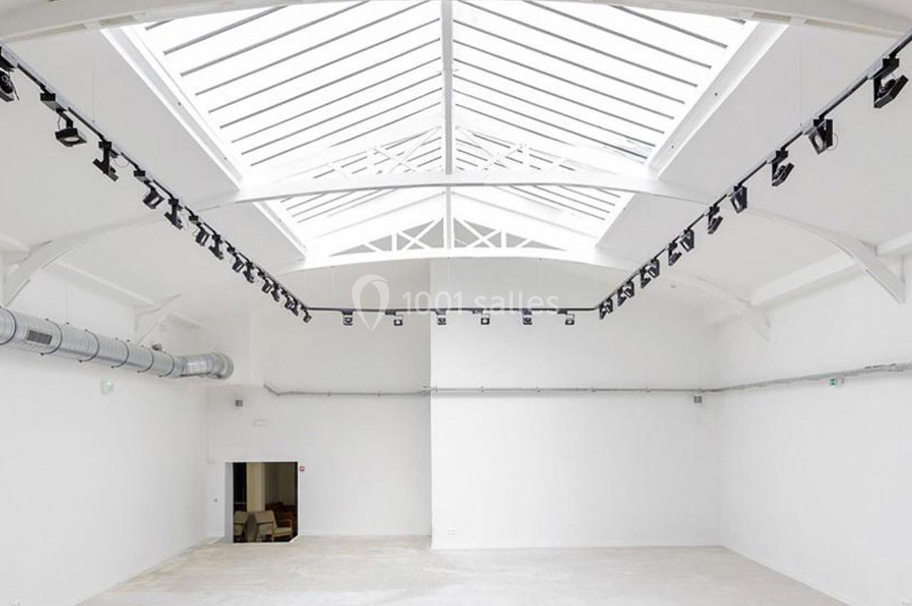 Vue intérieure d'un espace vide avec un plafond en verrière, des murs blancs et un éclairage suspendu.