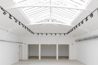 Salle lumineuse avec verrière, murs blancs, sol clair et mobilier minimaliste comprenant une table basse et un fauteuil.