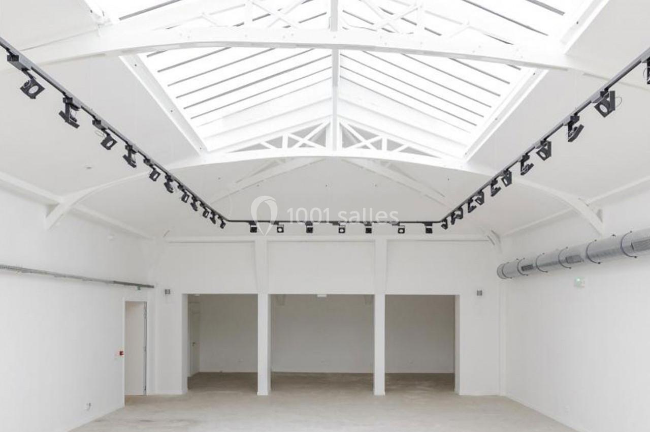 Vue intérieure d'un espace vide avec un plafond en verrière, des poutres blanches et des rails d'éclairage suspendus.