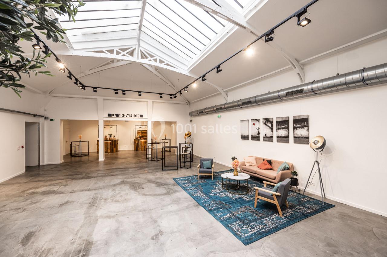 Salle lumineuse avec verrière, mobilier moderne, canapé, tapis bleu et décorations minimalistes.