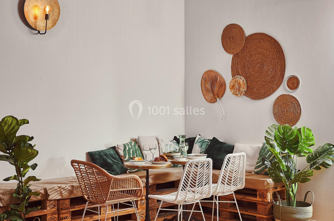 Coin salon chaleureux avec table en bois, chaises en rotin, coussins verts, plantes et décorations murales en osier.