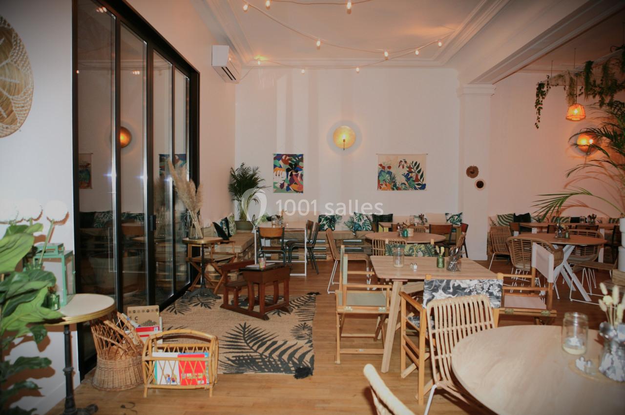 Salle lumineuse avec décoration tropicale, mobilier en bois, plantes vertes et guirlandes lumineuses suspendues.