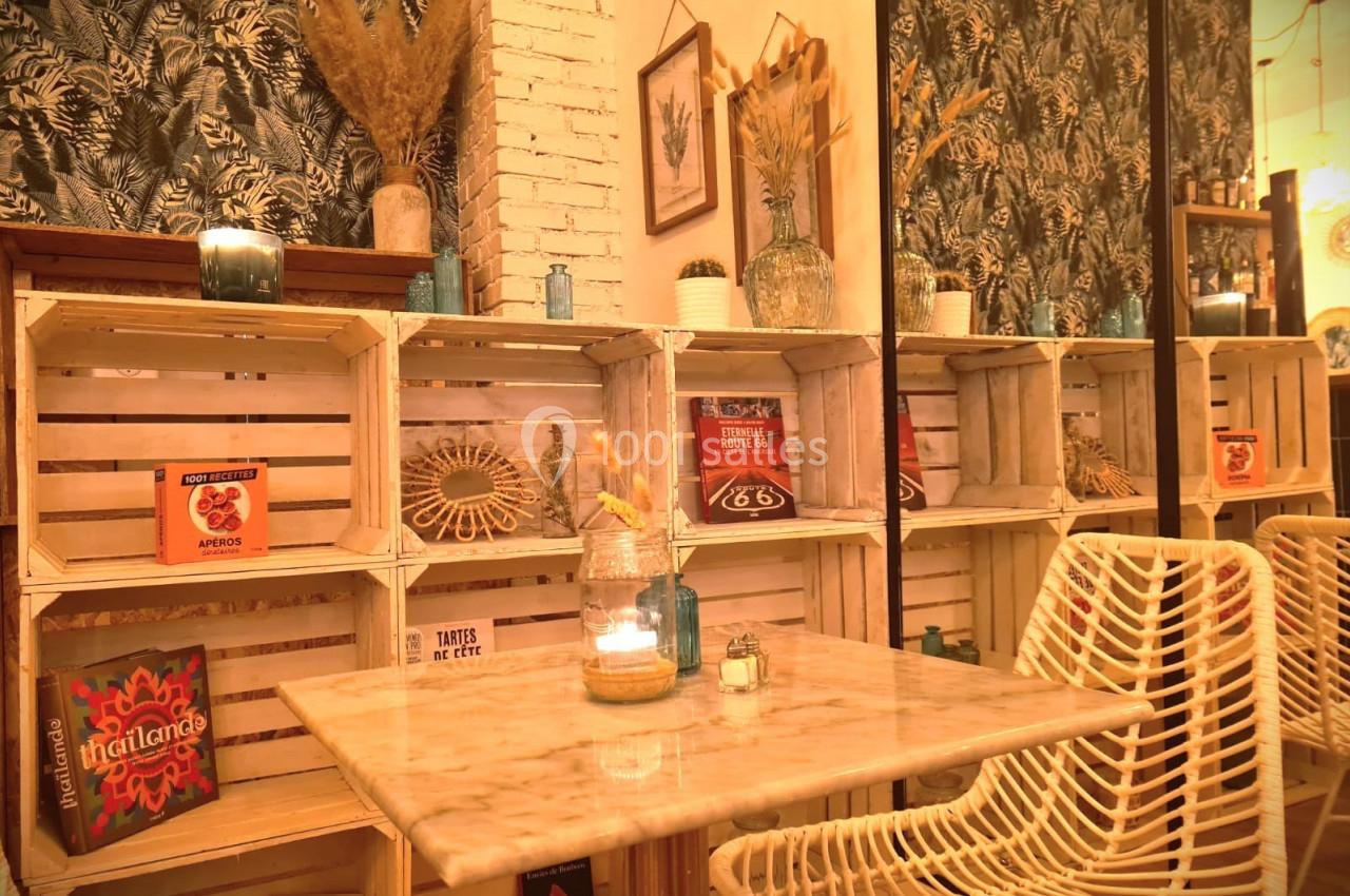 Table en marbre entourée de chaises en rotin, devant des étagères en caisses de bois décorées de livres et objets.