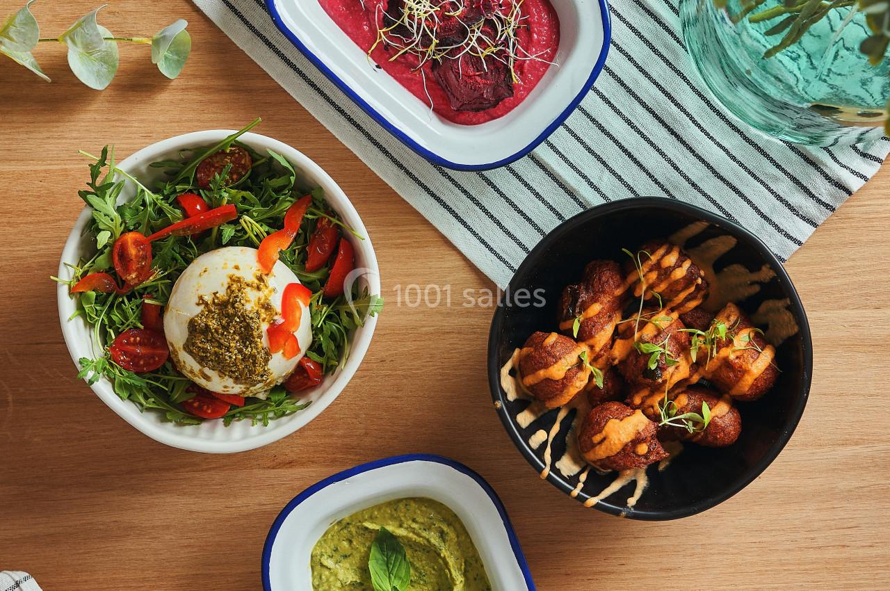 Quatre plats variés sur une table en bois, comprenant salade, houmous, brochettes et tartinade de betterave.