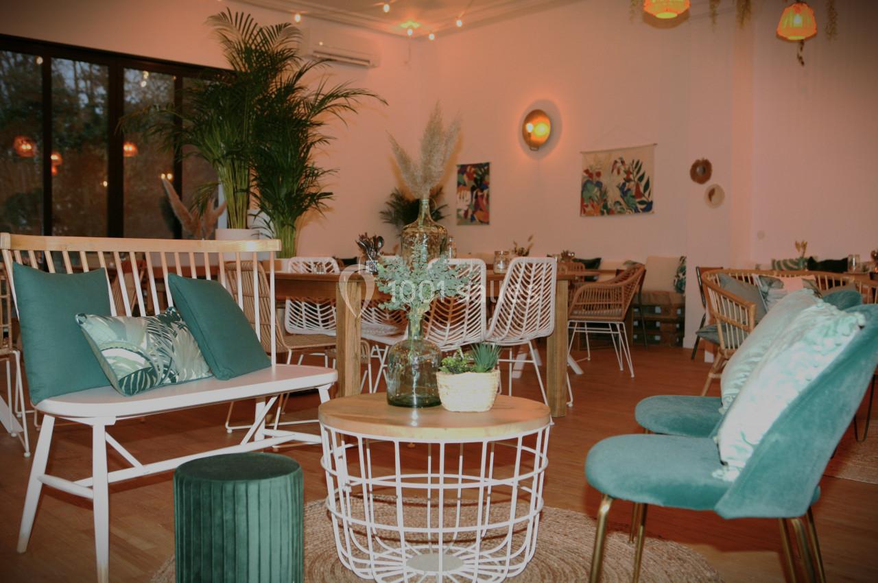 Salle lumineuse avec mobilier en bois et assises vertes, décorée de plantes et éclairée par des suspensions.