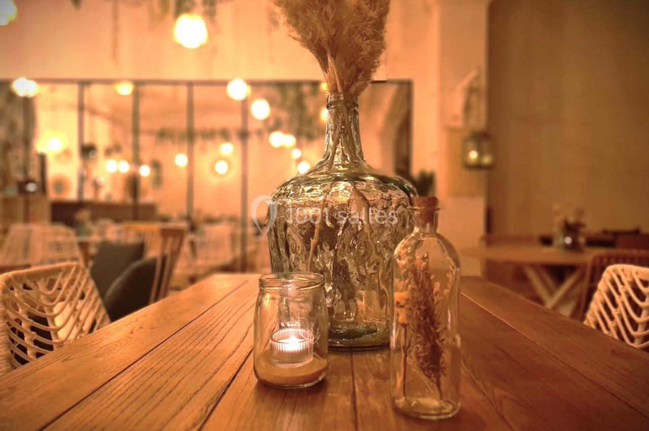 Vases en verre et bougie sur une table en bois dans un intérieur chaleureux avec éclairage tamisé.