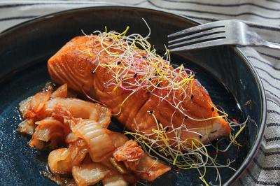 Saumon grillé garni de pousses, accompagné de kimchi, servi dans une assiette en céramique sur une nappe rayée.