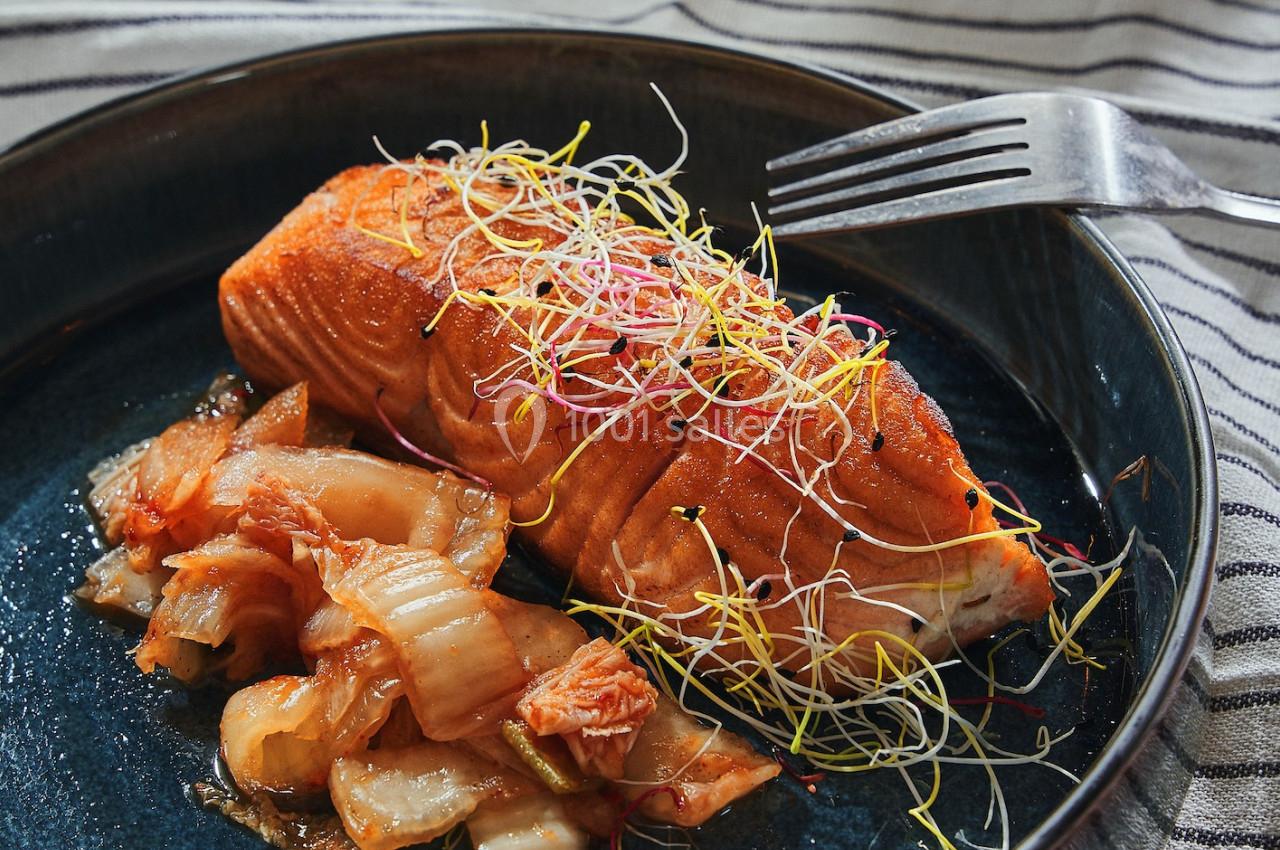 Saumon grillé garni de pousses, accompagné de kimchi, servi dans une assiette en céramique sur une nappe rayée.