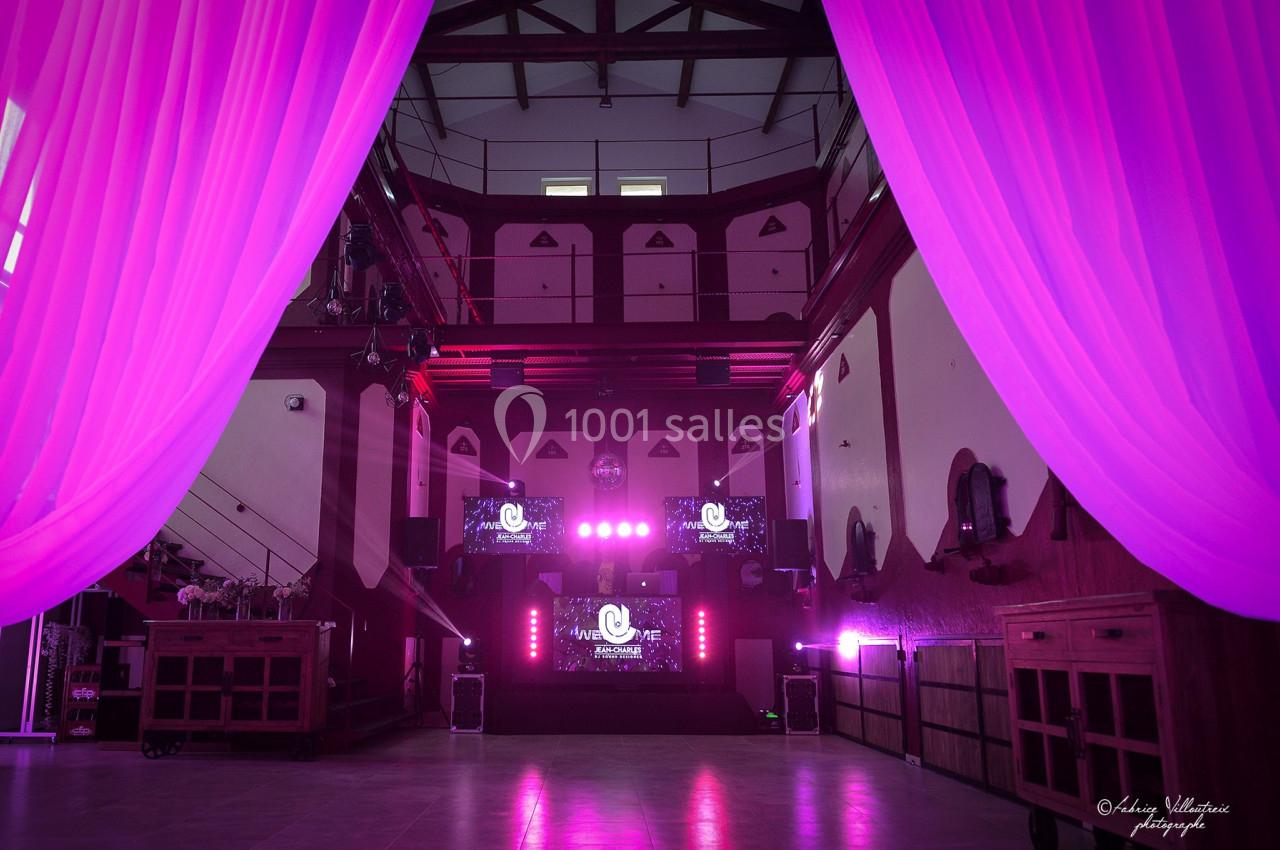 Salle de réception avec éclairage rose, rideaux ouverts au premier plan et écrans lumineux au fond.