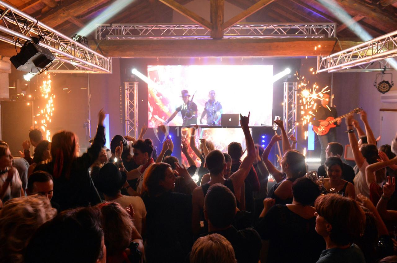 Foule dansant devant une scène avec DJ, éclairages colorés, effets pyrotechniques et ambiance festive.