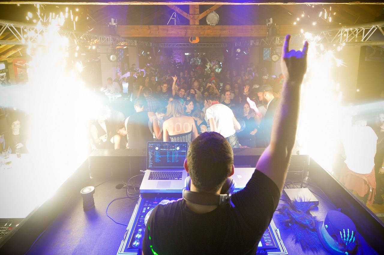 Un DJ anime une soirée en boîte de nuit, face à une foule dansante et des effets lumineux spectaculaires.