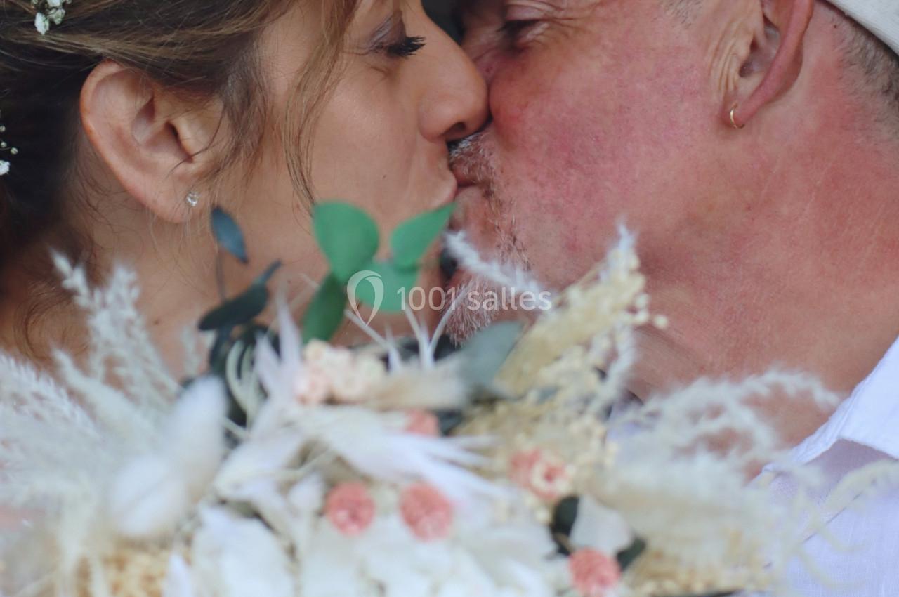 Un couple s'embrasse tendrement, un bouquet de fleurs aux tons pastel au premier plan.