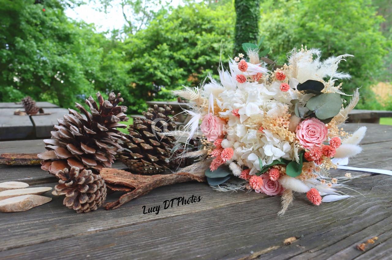 Bouquet de fleurs séchées et pommes de pin disposés sur une table en bois dans un environnement extérieur verdoyant.