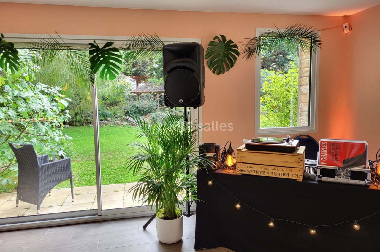 Table de DJ avec platine vinyle et enceintes près d'une baie vitrée donnant sur un jardin verdoyant.