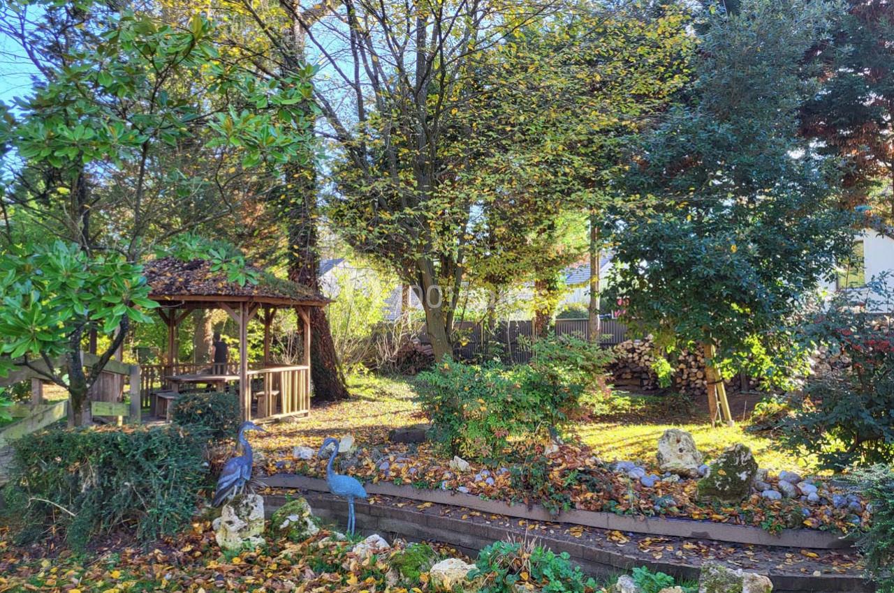 Jardin arboré en automne avec une tonnelle en bois, des statues d'oiseaux et un parterre couvert de feuilles.