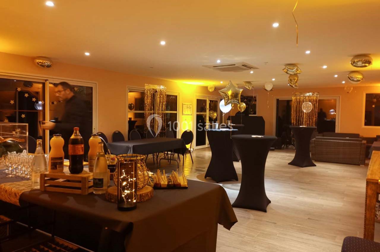 Salle décorée pour un événement avec tables hautes, ballons dorés et buffet disposé sur une table.