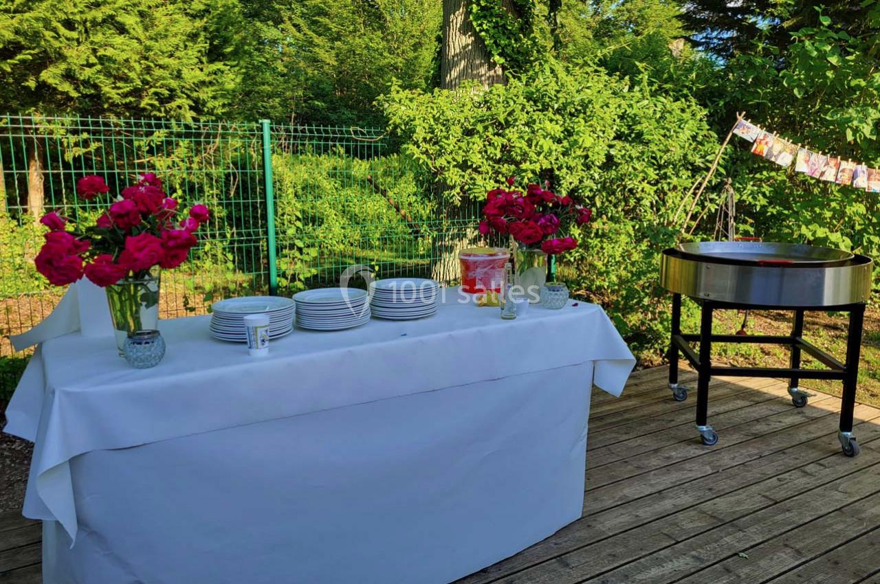 Table dressée en extérieur avec vaisselle blanche, bouquets de fleurs rouges et un barbecue à proximité.