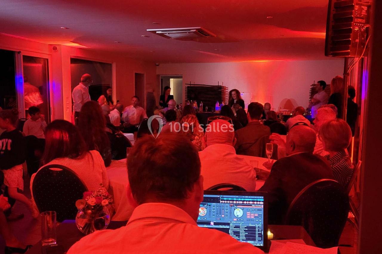 Groupe de personnes assises et debout dans une salle éclairée de lumières rouges, avec un DJ en arrière-plan.