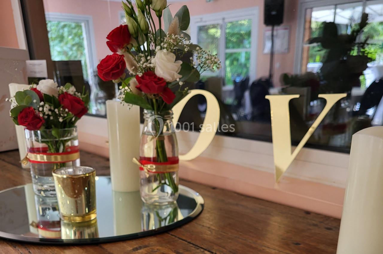 Bouquets de roses rouges et blanches dans des vases décorés, posés sur un miroir avec une bougie dorée.