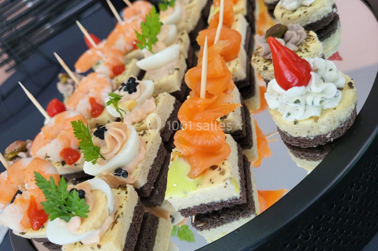 Plateau de canapés variés avec saumon fumé, œufs, fromage et décorations colorées sur un miroir.