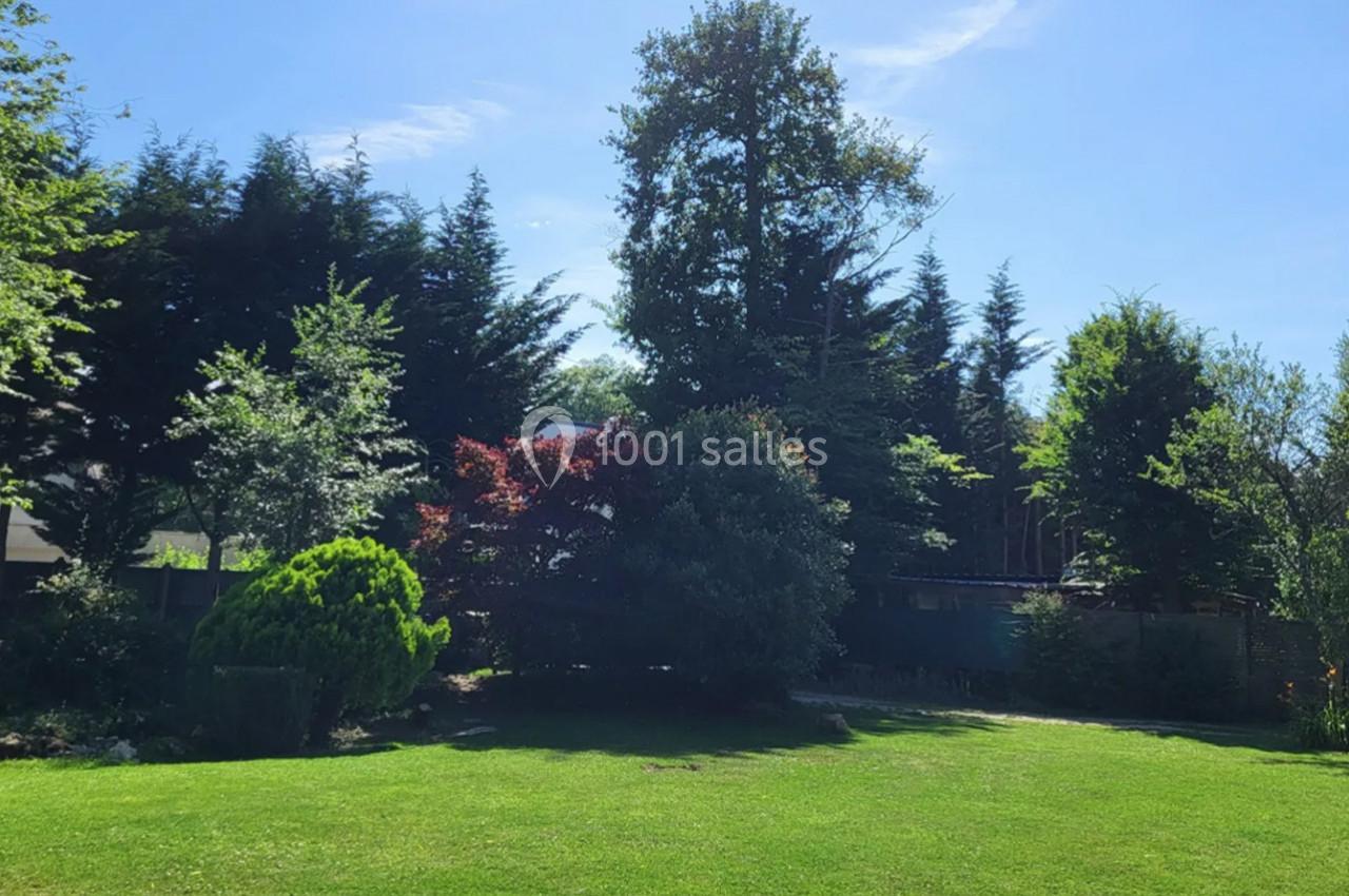 Pelouse verdoyante entourée d'arbres et d'arbustes sous un ciel bleu dégagé.