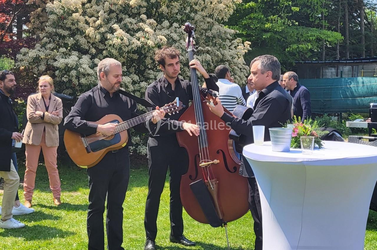Trois musiciens jouent de la guitare, de la contrebasse et de l'accordéon lors d'un événement en plein air.
