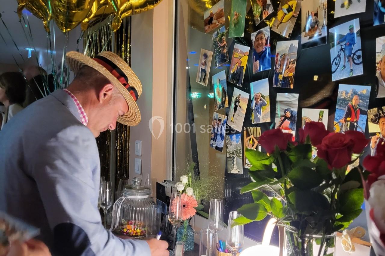 Un homme écrit dans un livre d'or lors d'un événement, entouré de ballons dorés, photos et fleurs.