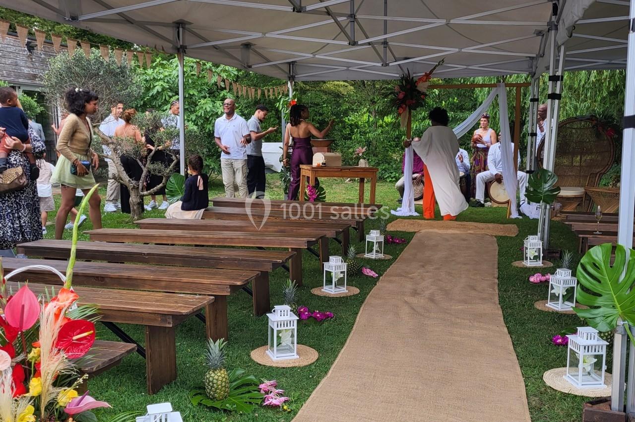 Cérémonie en extérieur sous une tente, avec allée en jute, bancs en bois et décorations tropicales.