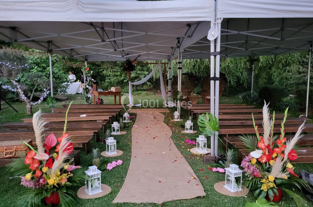 Allée décorée de fleurs et lanternes menant à une arche sous des tonnelles dans un jardin pour une cérémonie.