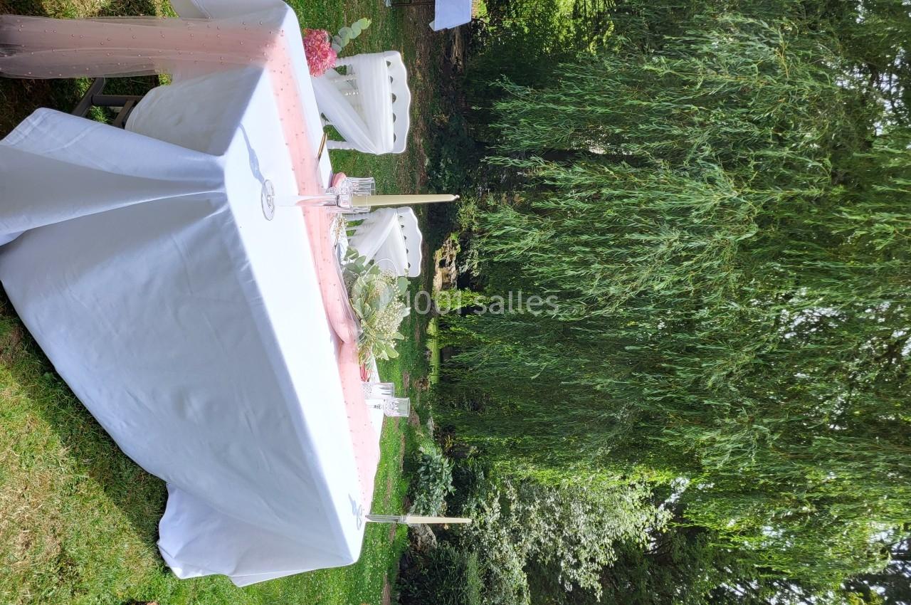 Table décorée avec une nappe blanche et un chemin de table rose, installée dans un jardin verdoyant.