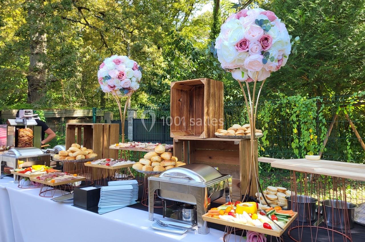 Buffet en plein air avec pains, légumes, plats chauds et décorations florales sur une table blanche.