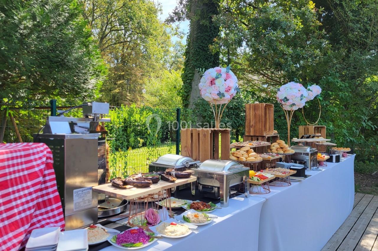 Buffet en plein air avec plats variés, décoré de ballons et de caisses en bois, entouré de verdure.