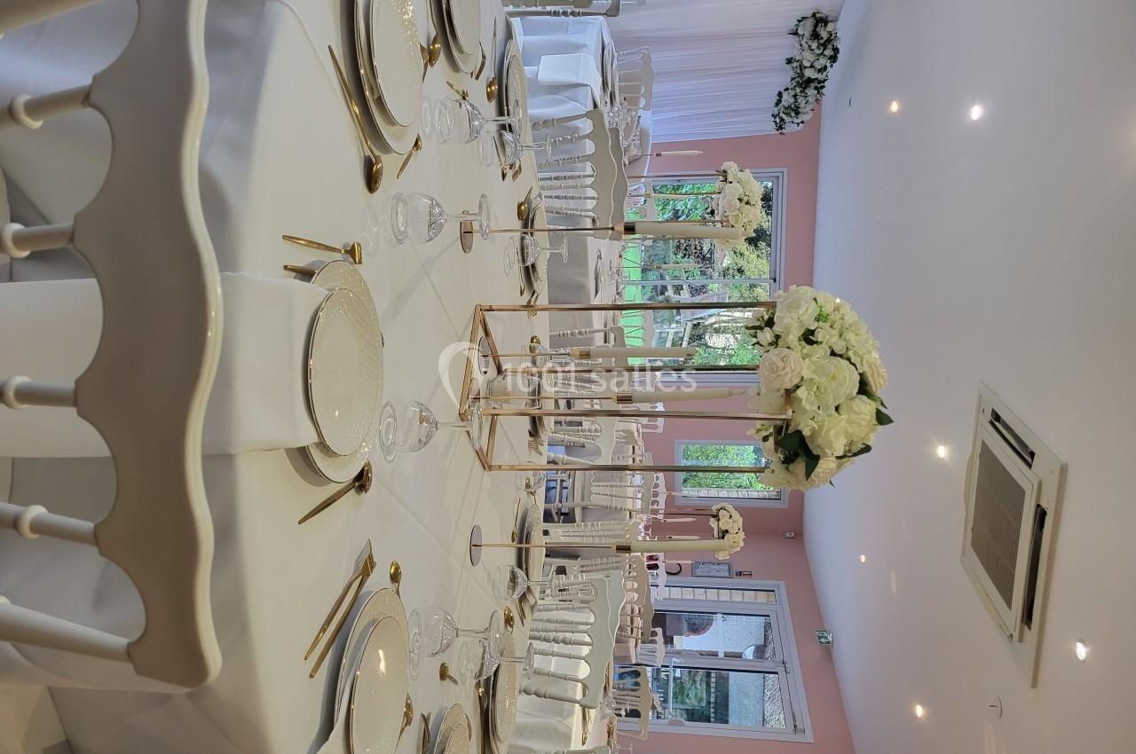 Salle de réception décorée avec des tables rondes, nappes blanches, vaisselle élégante et centres de table fleuris.