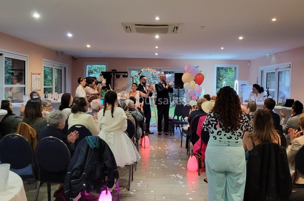 Un couple se tient debout devant des invités assis lors d'une cérémonie dans une salle décorée de ballons.