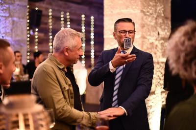 Un homme en costume montre un jeu de cartes à une jeune fille concentrée, assise à une table dans un décor en briques.