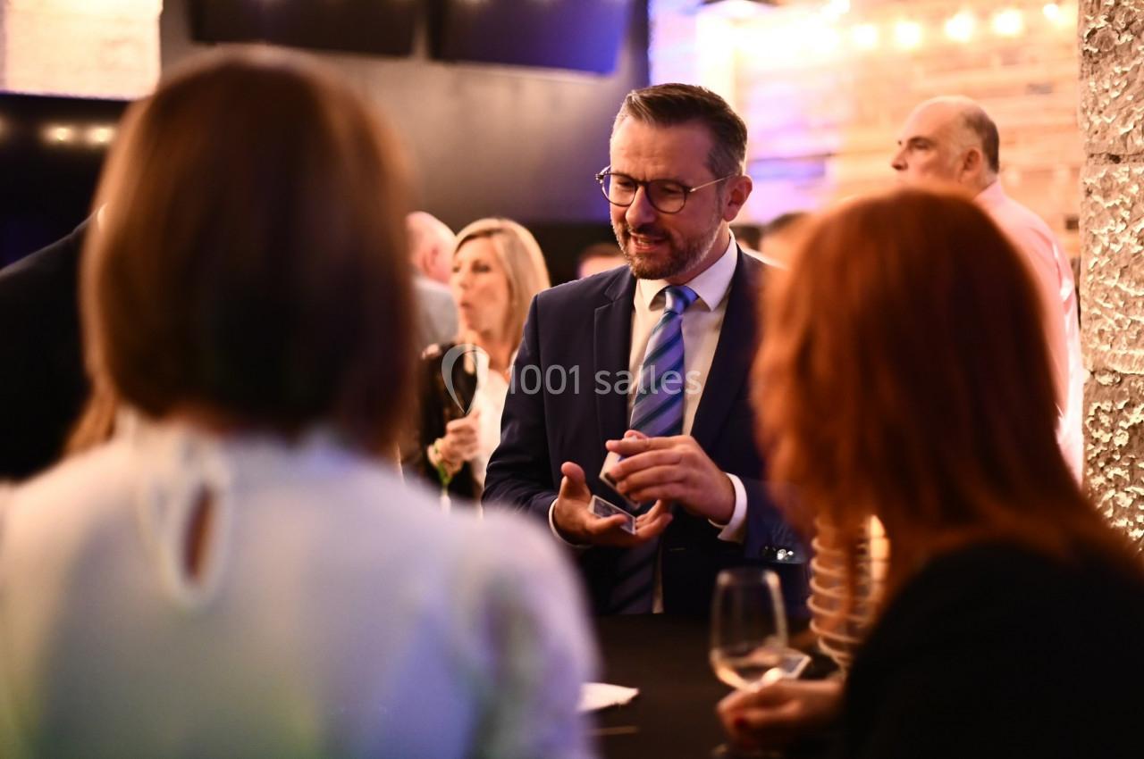 Un homme en costume discute avec deux personnes lors d'un événement social dans un espace éclairé.