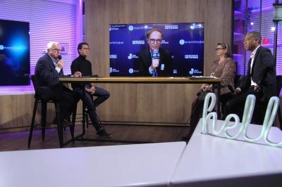 Cinq personnes discutent sur un plateau télévisé, avec un écran diffusant une intervention en visioconférence.