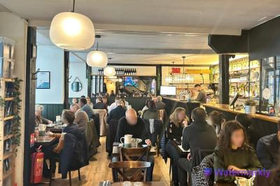 Intérieur d'un café animé avec des clients attablés et un comptoir en arrière-plan.