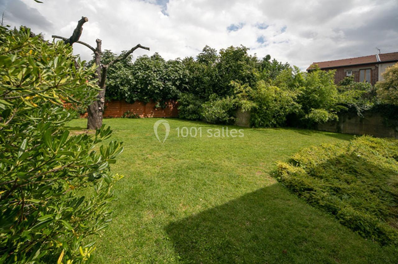Jardin verdoyant avec pelouse, arbres et haies, sous un ciel partiellement nuageux.