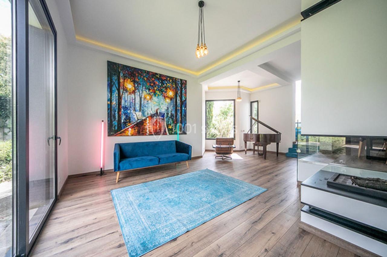 Salon lumineux avec un canapé bleu, un tapis turquoise, un piano et une grande peinture colorée sur le mur.