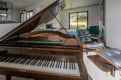Jardin avec pelouse, arbre taillé, haies verdoyantes et maison moderne en arrière-plan sous un ciel partiellement nuageux.
