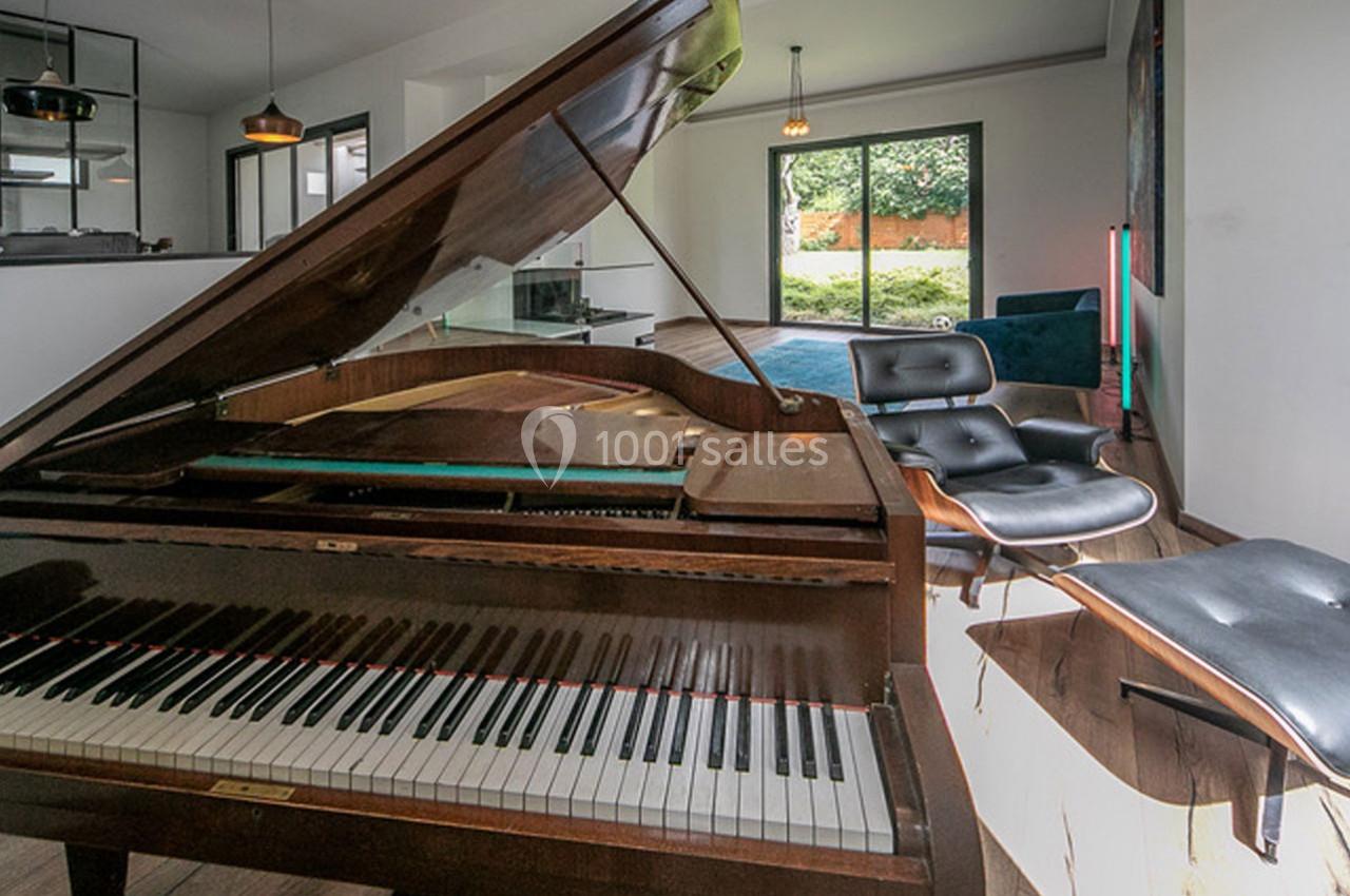Un piano à queue en bois dans un salon lumineux avec fauteuils modernes et vue sur un jardin.